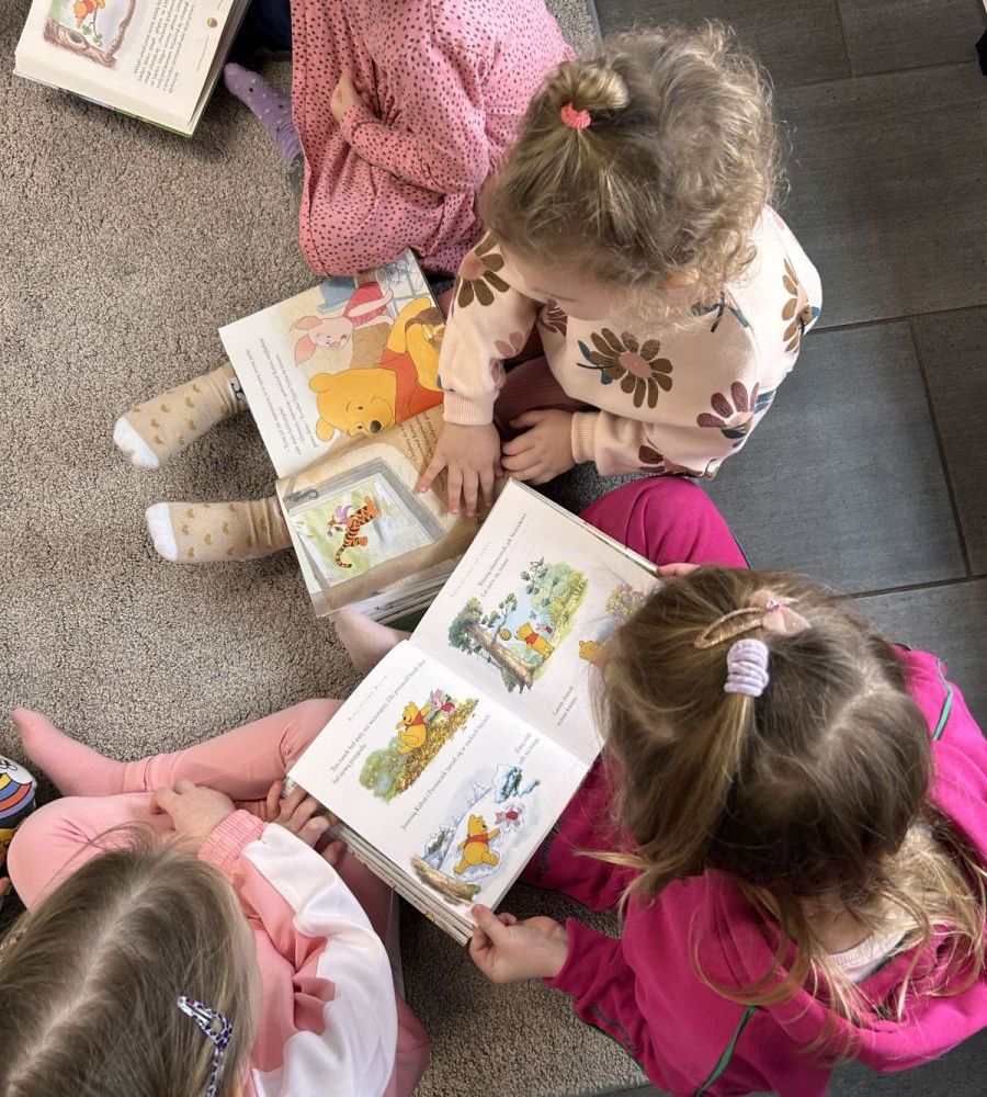 Dzieci na dywanie oglądają książki o Kubusiu Puchatku